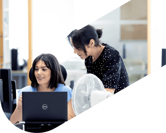 two women in an office setting, one on a laptop